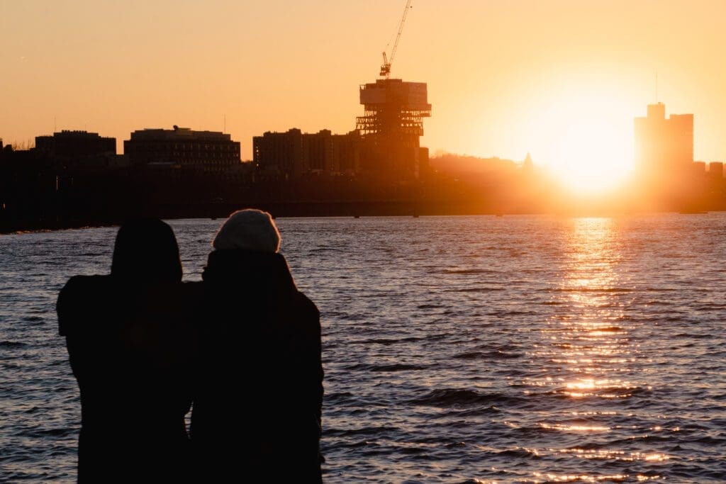 A couple stands infront of the Charles River. 