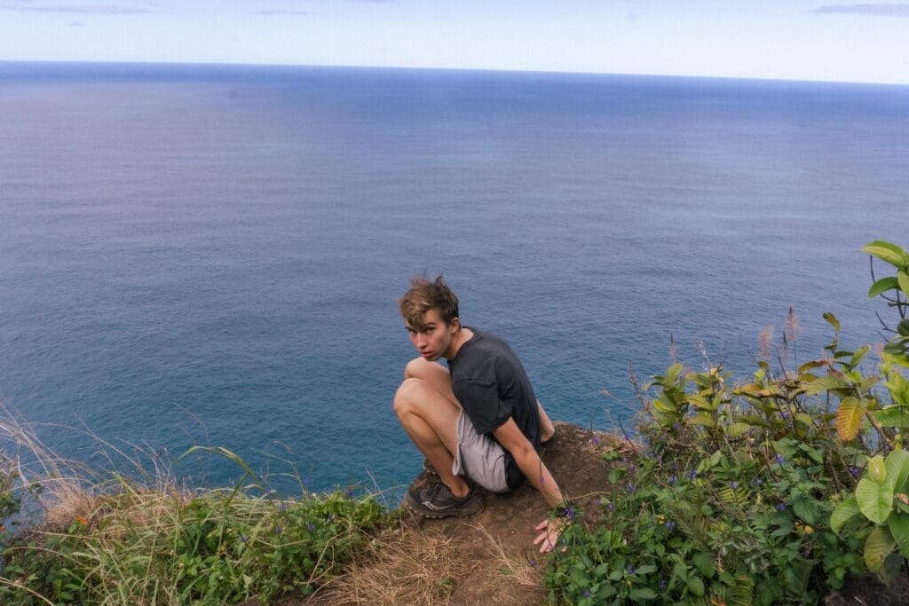 In Kauai, on the Napali Coast, noah poses on a ledge overlooking the ocean.